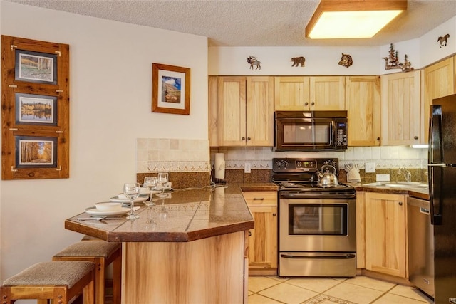 kitchen with tile counters, light brown cabinetry, black appliances, a peninsula, and a kitchen bar
