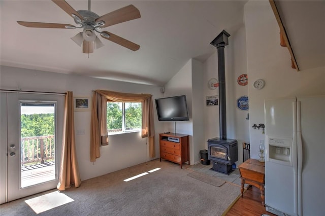 living room featuring vaulted ceiling, a wood stove, light colored carpet, and ceiling fan