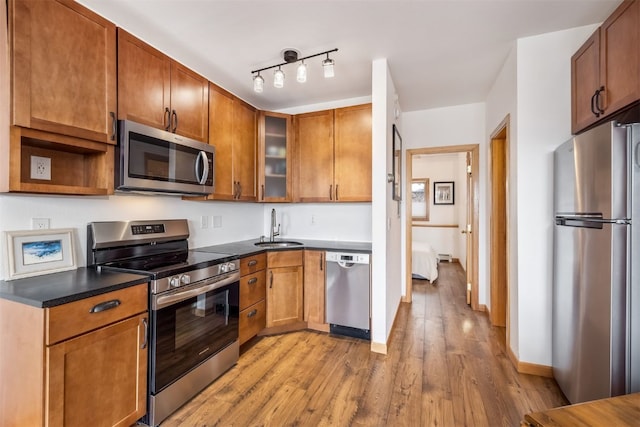 kitchen featuring dark countertops, glass insert cabinets, light wood-style floors, a sink, and appliances with stainless steel finishes