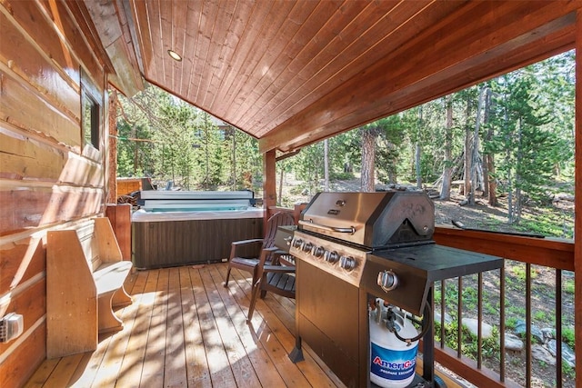 wooden terrace with a forest view, a hot tub, and area for grilling