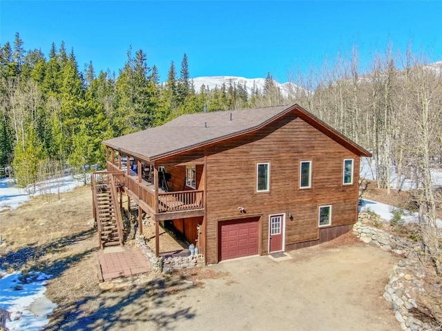 back of property with a mountain view, a view of trees, stairs, and a garage