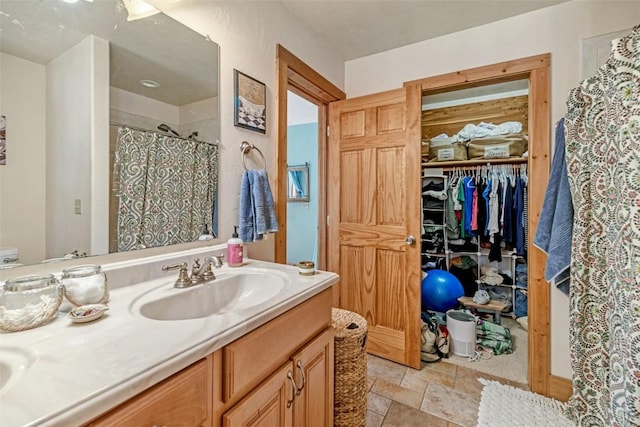 bathroom with stone finish floor, a spacious closet, vanity, and a shower with curtain