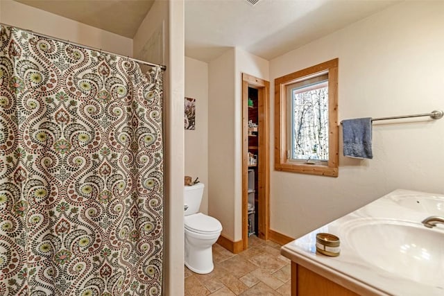 bathroom featuring curtained shower, stone finish floor, double vanity, toilet, and a sink