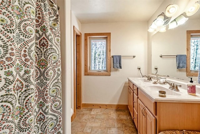 full bathroom with double vanity, stone finish flooring, baseboards, and a sink