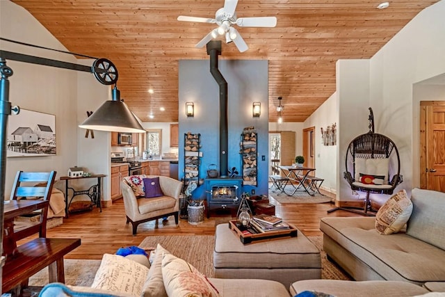living room with vaulted ceiling, light wood-style floors, ceiling fan, a wood stove, and wooden ceiling