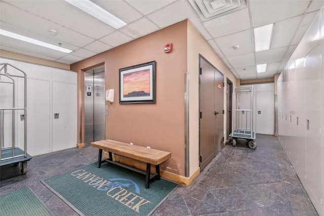 corridor featuring a drop ceiling, elevator, dark stone finish flooring, and baseboards
