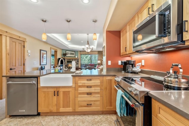 kitchen with appliances with stainless steel finishes, a sink, a peninsula, hanging light fixtures, and a raised ceiling