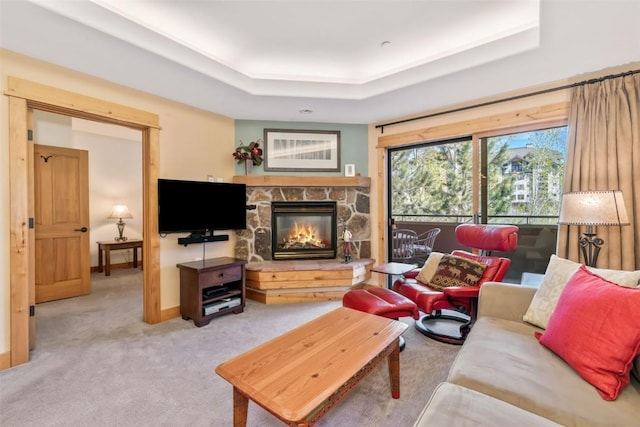 carpeted living area featuring a stone fireplace, a tray ceiling, and baseboards
