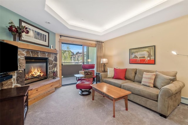 carpeted living room featuring a stone fireplace and a tray ceiling