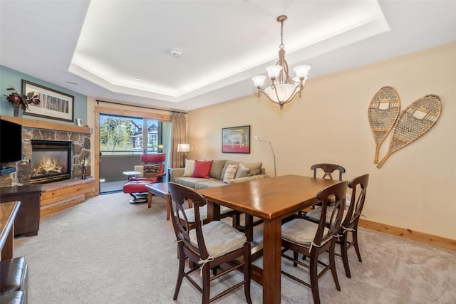 dining room featuring a raised ceiling, light colored carpet, a fireplace, a chandelier, and baseboards