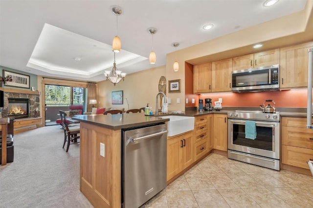 kitchen with stainless steel appliances, a tray ceiling, a sink, open floor plan, and light brown cabinets