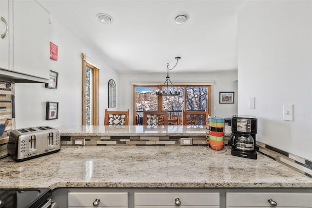 kitchen with a peninsula, a toaster, electric range, a chandelier, and light stone countertops