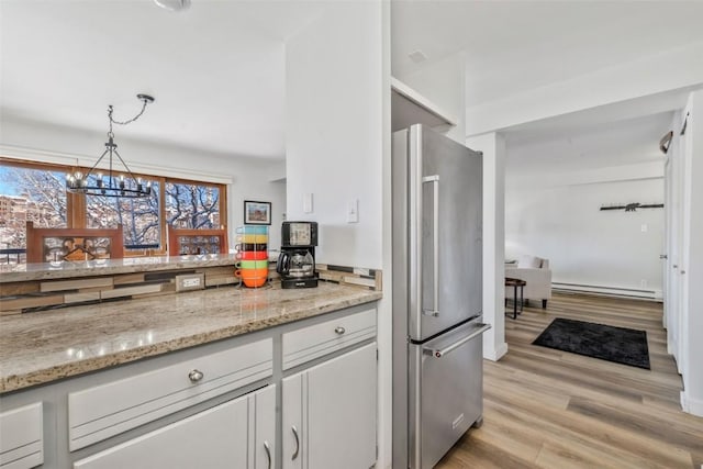 kitchen featuring white cabinets, freestanding refrigerator, a notable chandelier, light wood-style floors, and baseboard heating