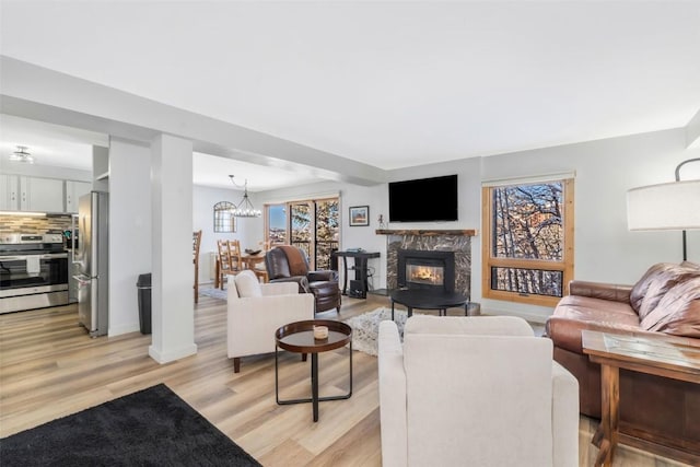 living area with a high end fireplace, baseboards, a notable chandelier, and light wood-type flooring