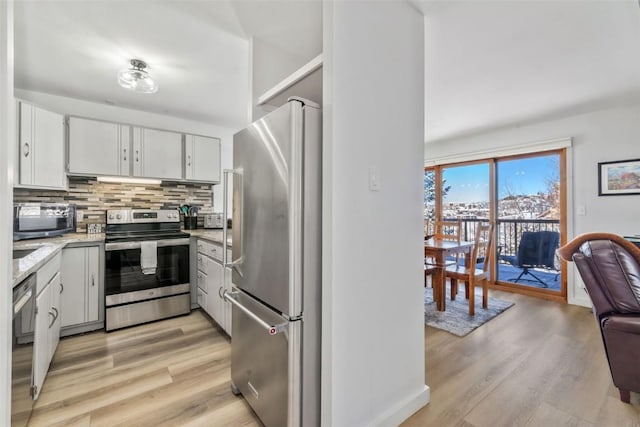 kitchen with stainless steel appliances, backsplash, light wood-style floors, and white cabinetry