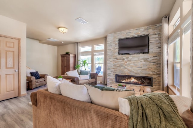 living room with light wood-style flooring, visible vents, and a stone fireplace