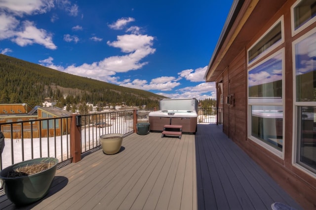 deck featuring a forest view, a hot tub, and a mountain view