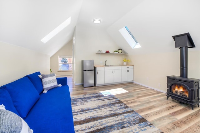 living room featuring lofted ceiling with skylight, a wood stove, light wood-style floors, and baseboards