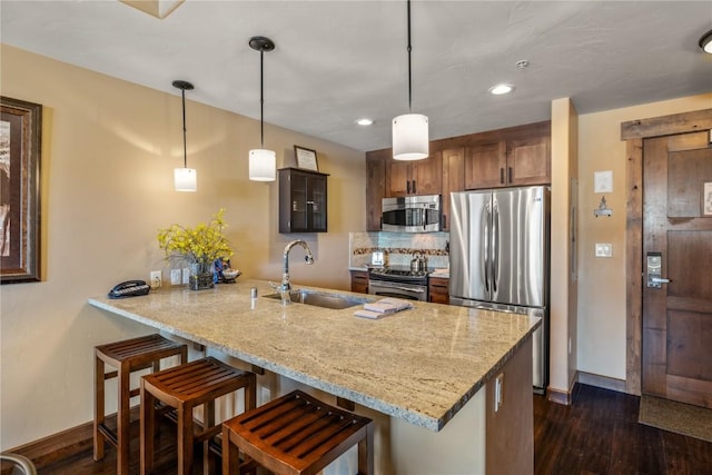 kitchen with a sink, dark wood-type flooring, baseboards, a peninsula, and appliances with stainless steel finishes