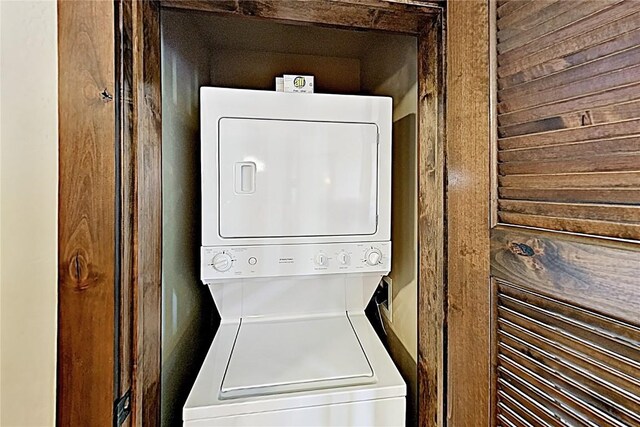 clothes washing area featuring wooden walls, stacked washing maching and dryer, and laundry area