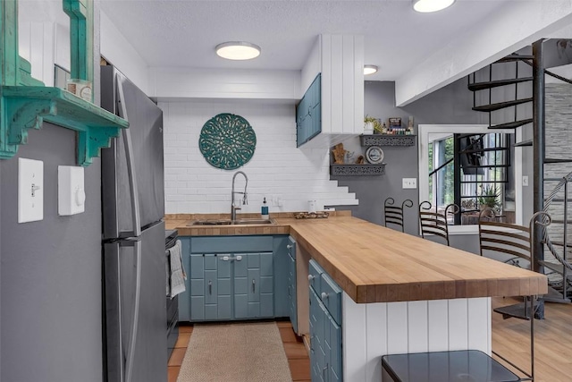 136 Lance Ln Unit 2, Breckenridge, CO 80424 - kitchen with butcher block countertops, blue cabinetry, freestanding refrigerator, light wood finished floors, and tasteful backsplash