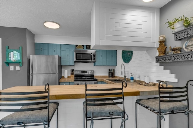 136 Lance Ln Unit 2, Breckenridge, CO 80424 - kitchen with appliances with stainless steel finishes, butcher block counters, tasteful backsplash, a kitchen bar, and blue cabinetry
