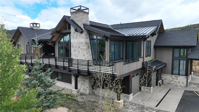 rear view of house featuring a standing seam roof, stone siding, a chimney, metal roof, and a garage