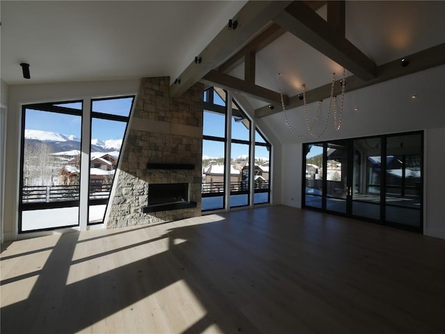 unfurnished living room with a stone fireplace, a healthy amount of sunlight, wood finished floors, and beam ceiling
