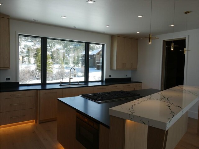kitchen with stainless steel gas stovetop, built in microwave, light wood finished floors, a sink, and a center island