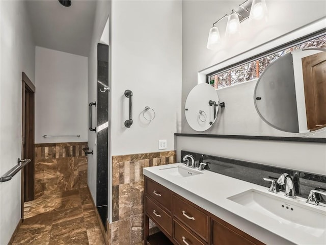 full bathroom with tile walls, a walk in shower, wainscoting, and a sink