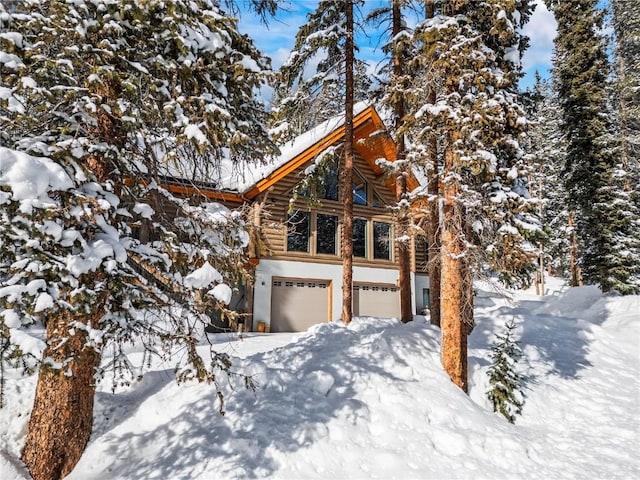 snow covered property with log siding and a garage