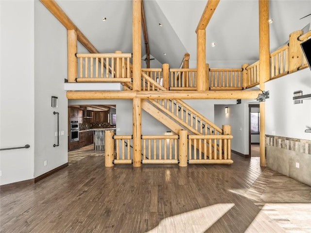 unfurnished living room featuring baseboards, beamed ceiling, stairway, high vaulted ceiling, and wood-type flooring