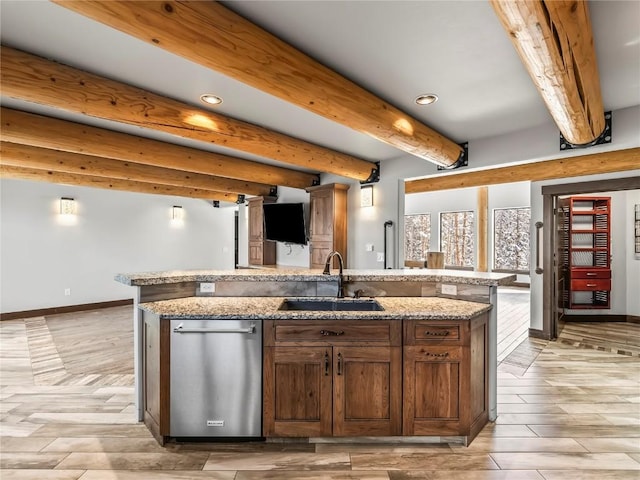kitchen with light wood finished floors, stainless steel dishwasher, a sink, baseboards, and a kitchen island with sink