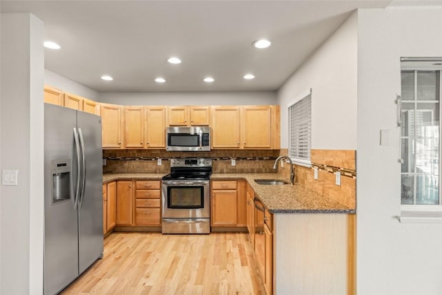 kitchen with light brown cabinets, stone counters, a sink, light wood-style floors, and appliances with stainless steel finishes