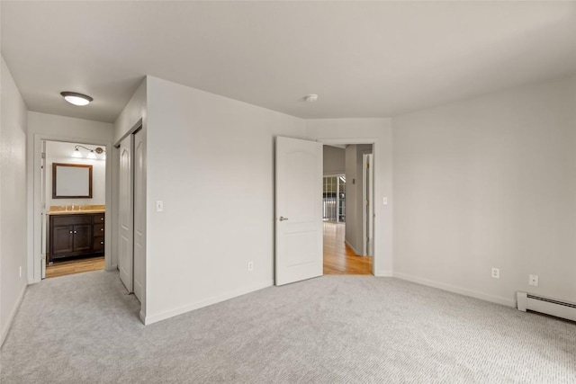 unfurnished bedroom with a sink, light colored carpet, ensuite bath, a baseboard radiator, and baseboards