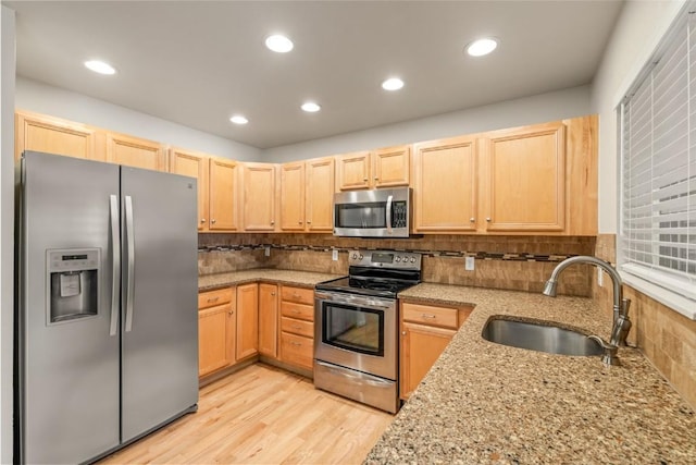kitchen featuring light wood finished floors, a sink, light brown cabinets, backsplash, and appliances with stainless steel finishes