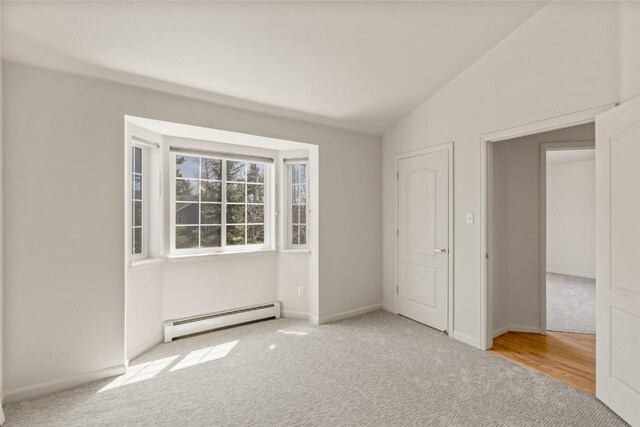 spare room with a baseboard heating unit, carpet flooring, baseboards, and lofted ceiling