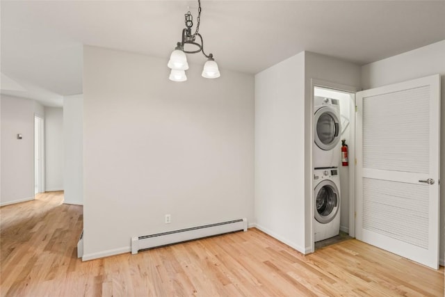 laundry area with a baseboard radiator, baseboards, light wood finished floors, stacked washing maching and dryer, and laundry area