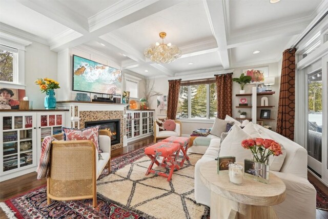 living area featuring a glass covered fireplace, ornamental molding, coffered ceiling, and wood finished floors
