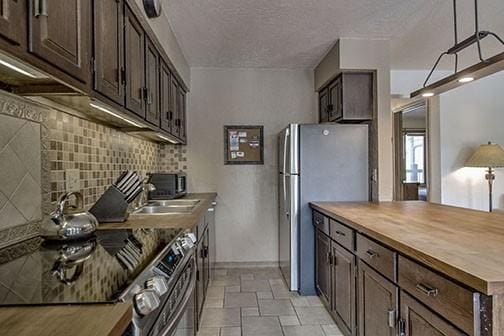 820 Columbine Rd Unit 10, Breckenridge, CO 80424 - kitchen featuring butcher block countertops, decorative backsplash, dark brown cabinetry, a textured ceiling, and appliances with stainless steel finishes