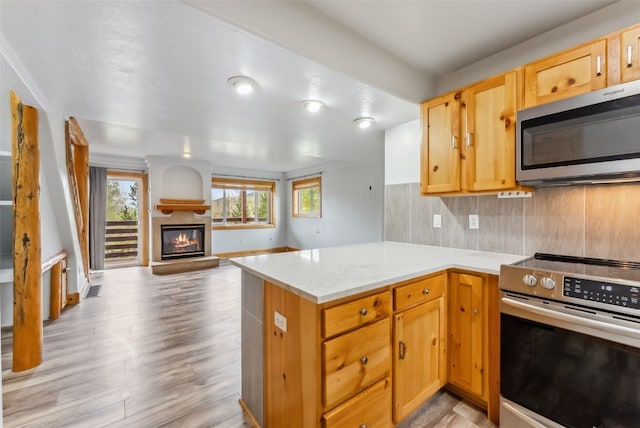 80 Cove Blvd Unit 103, Dillon, CO 80435 - kitchen featuring appliances with stainless steel finishes, open floor plan, a peninsula, a glass covered fireplace, and light wood-type flooring