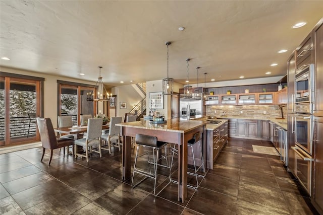 kitchen with tasteful backsplash, a kitchen island, light stone counters, built in appliances, and pendant lighting