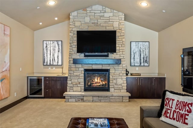 living room with wine cooler, a stone fireplace, carpet floors, baseboards, and vaulted ceiling