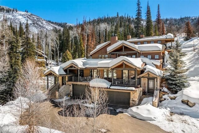 rustic home featuring stone siding, a view of trees, and an attached garage