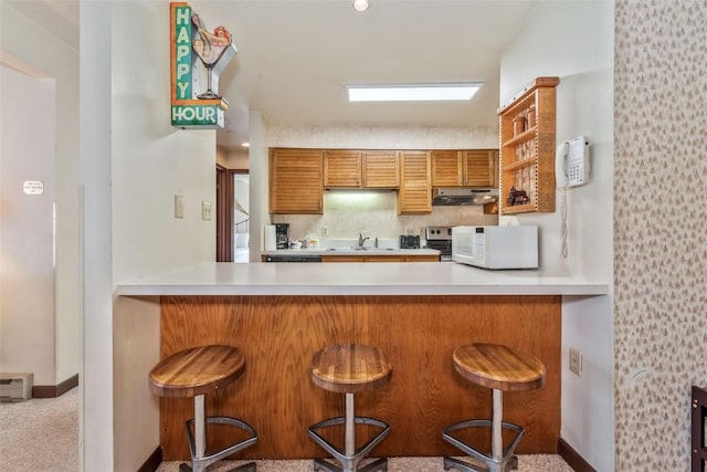 2015 Walton Creek Rd Unit 114, Steamboat Springs, CO 80487 - kitchen featuring a sink, under cabinet range hood, a peninsula, and white microwave