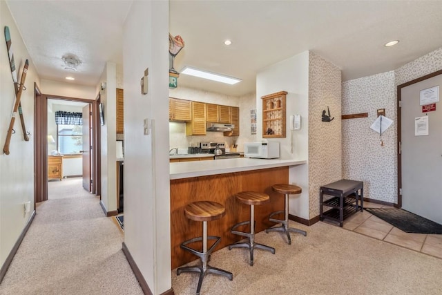 2015 Walton Creek Rd Unit 114, Steamboat Springs, CO 80487 - kitchen featuring electric range, light colored carpet, a breakfast bar area, white microwave, and under cabinet range hood