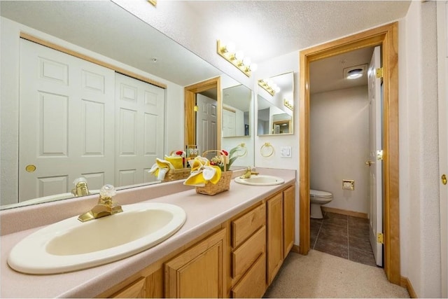bathroom featuring double vanity, toilet, baseboards, and a sink