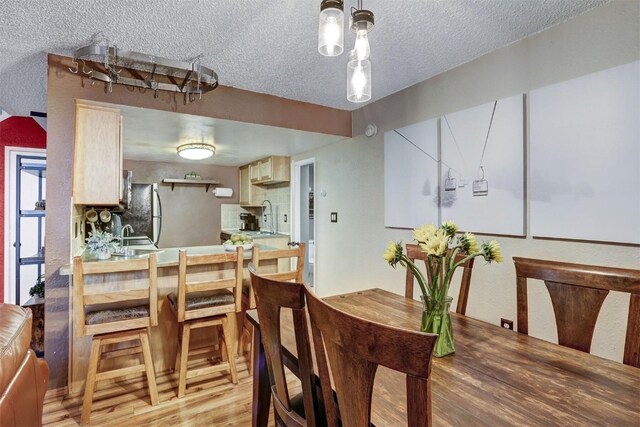 dining area featuring sink, a textured ceiling, and light hardwood / wood-style flooring