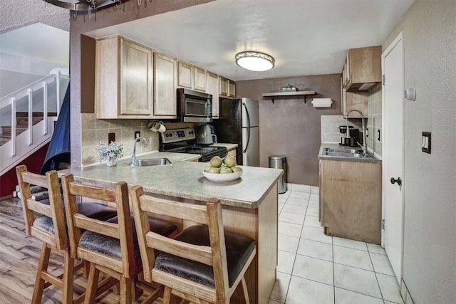 kitchen with light brown cabinets, backsplash, sink, appliances with stainless steel finishes, and light tile patterned flooring