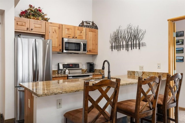 kitchen with stainless steel appliances, a breakfast bar, light stone counters, and a peninsula